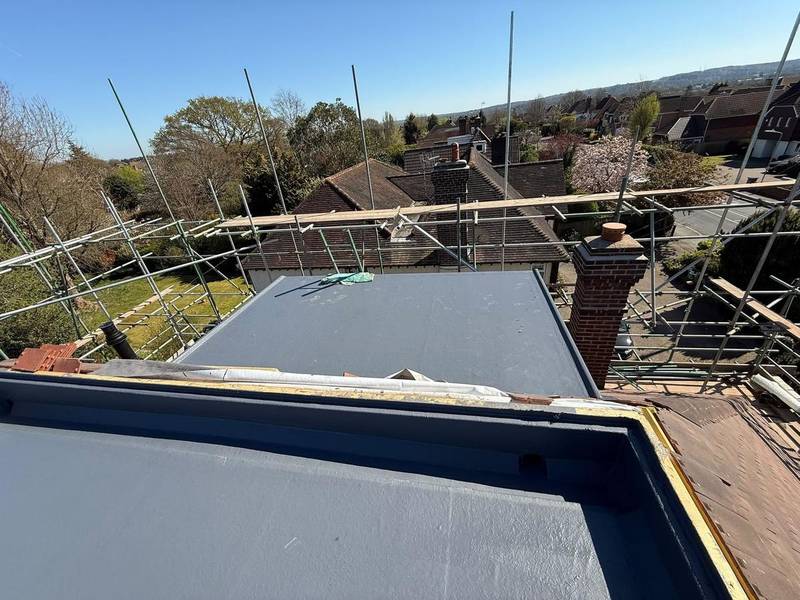 Newly finished grey flat roof with edge trims, viewed from the scaffold