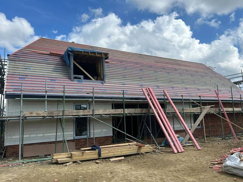 House part-way through a re-roof with scaffold, new battens and membrane around a dormer