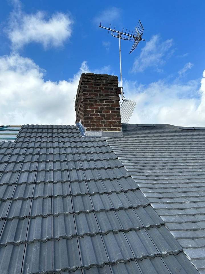 Grey concrete tile roof with a brick chimney stack against blue sky